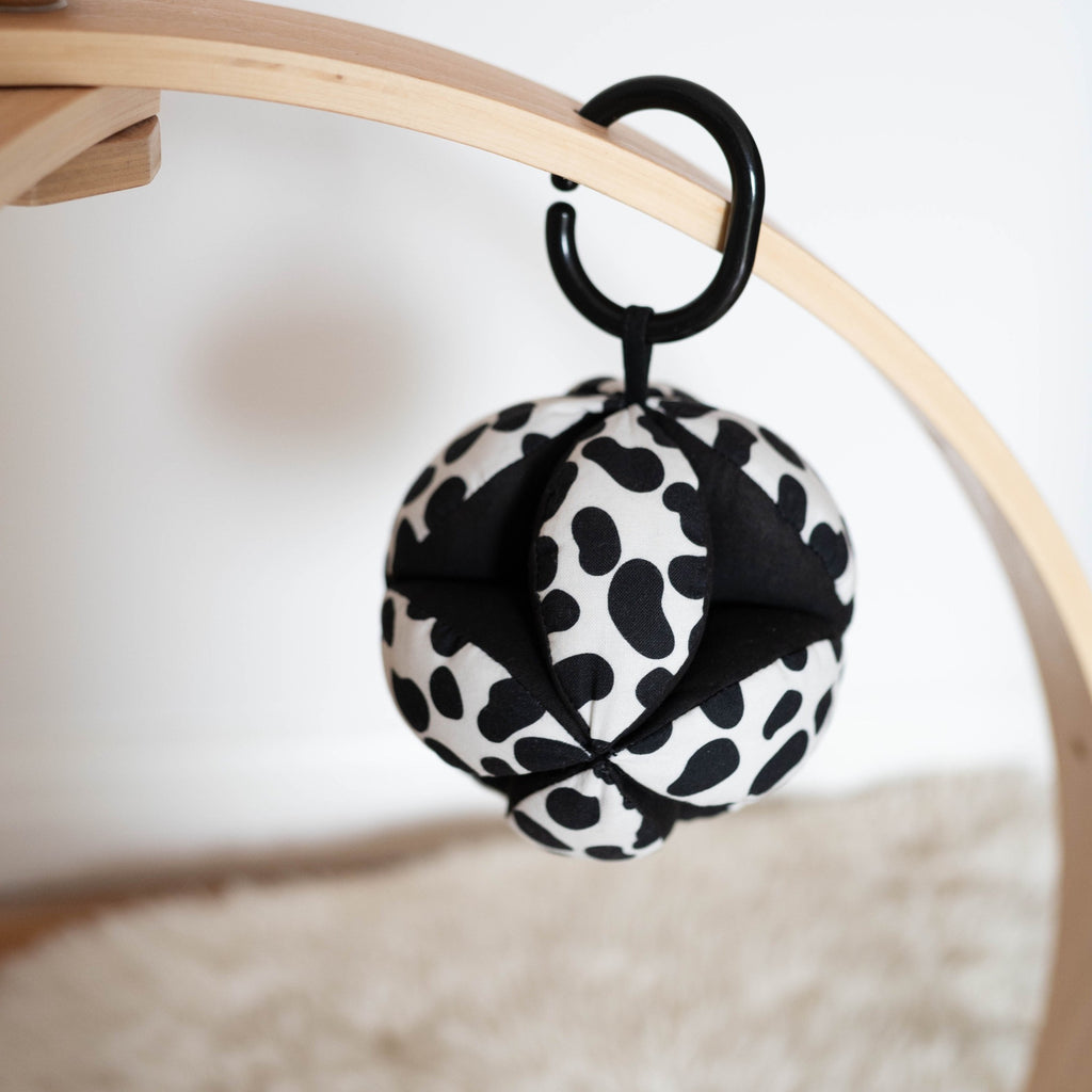 a sensory grasp ball in Dalmatian print hanging on a wooden baby gym arch