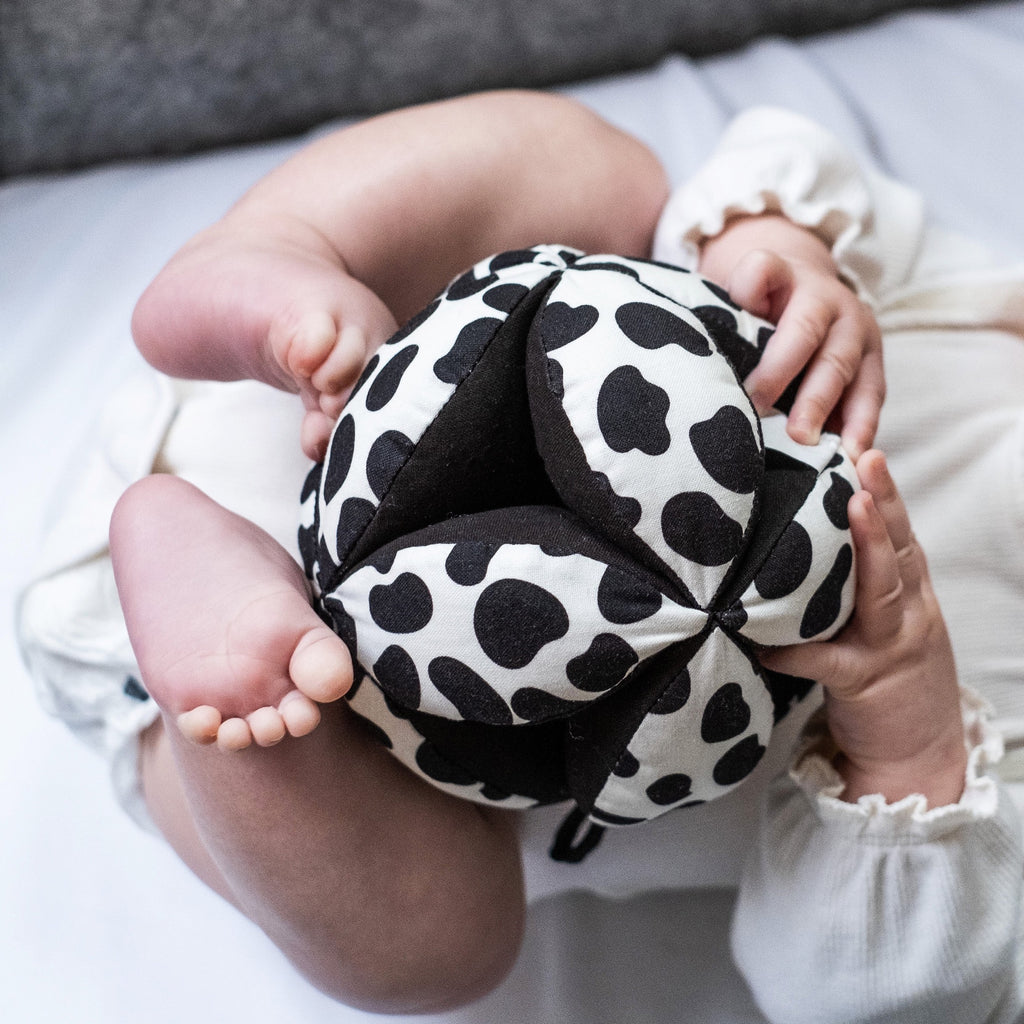 image of a baby lying on their back with the hands and feet grasping a dalamatian print sensory grab ball